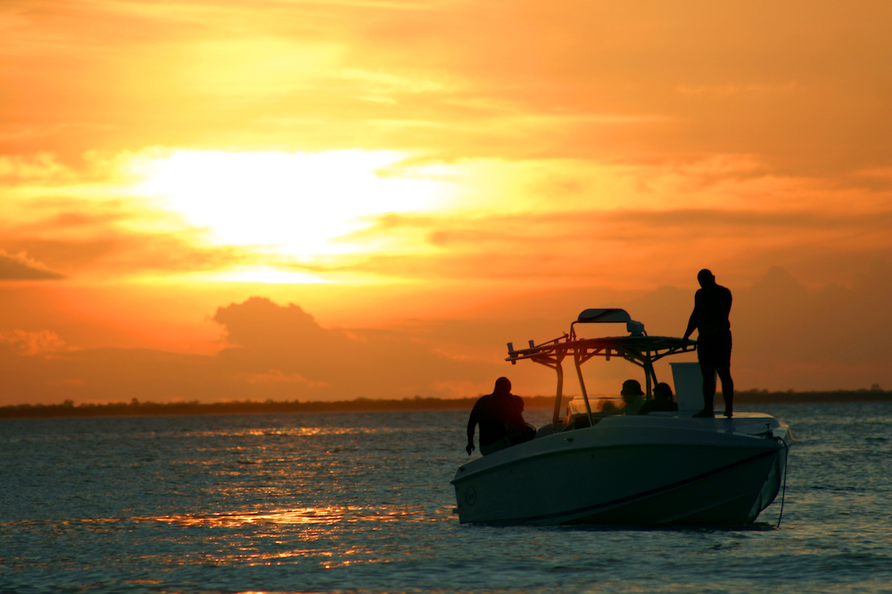 people standing on a fishing boat at sunset